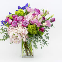 Tall pink and purple mixed flower arrangement in a clear rectangular glass vase