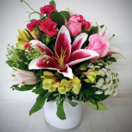 Mixed bouquet of pink roses, lilies, and carnations in a white vase