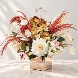 Mixed floral arrangement in a square metallic vase with cream and rust tones