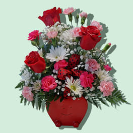 Red and pink flower arrangement in a red smiling pot