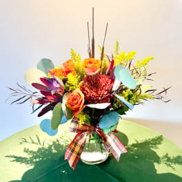 Orange roses and a red chrysanthemum in a glass vase with a plaid ribbon