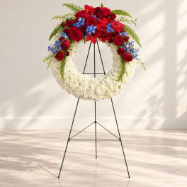 Floral wreath on a metal stand with red roses, white flowers, and blue accents