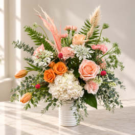 Mixed bouquet of peach, orange, and white flowers in a white vase