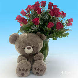 Red roses in a glass vase with a plush teddy bear in front