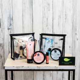 Two clear toiletry bags with assorted bath and body products on a table