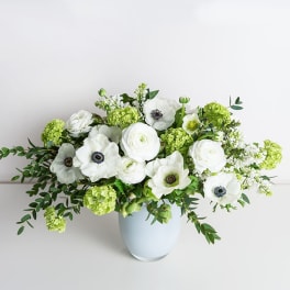White flowers and green blooms arranged in a pale blue vase