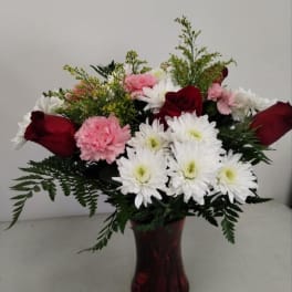 Arrangement of red roses, pink carnations, and white chrysanthemums in a red glass vase