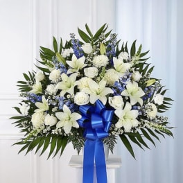 White lilies and roses with blue accents in a standing spray with a blue ribbon
