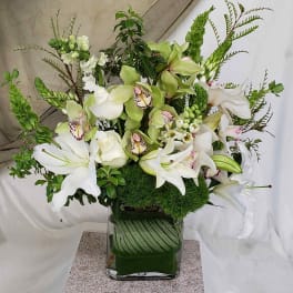 White lilies and green orchids arranged in a square glass vase.