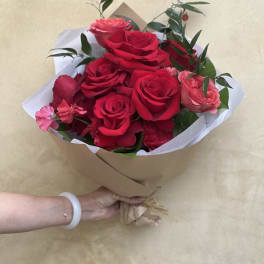 Handheld bouquet of red and pink roses wrapped in brown paper