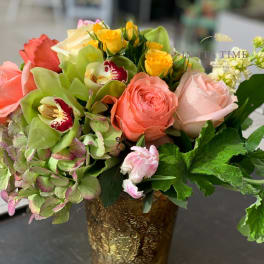 Mixed bouquet of roses, orchids, and hydrangeas in a gold vase