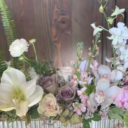 Pastel floral arrangement with white lilies, roses, and orchids in a rustic container
