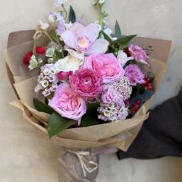 Pink and white bouquet with roses and orchids wrapped in brown paper
