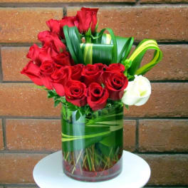 Red roses arranged in a glass vase with green ribbon accents