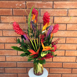 Tall tropical bouquet in a glass vase with red, orange, and purple blooms