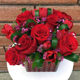 Red roses and pink accent flowers in a square vase