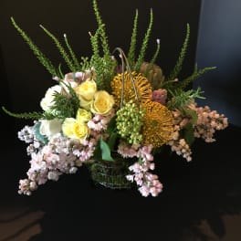 Mixed floral arrangement with yellow roses and pink blooms in a wire basket