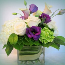White roses, purple calla lilies, and hydrangeas in a glass vase
