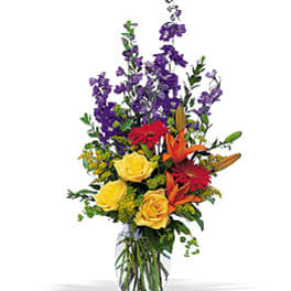 Tall mixed bouquet in a clear glass vase with yellow roses and purple flowers