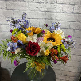 Mixed bouquet with sunflowers, roses, and blue flowers in a glass vase