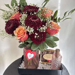 Bouquet of burgundy chrysanthemums and peach roses in a vase with chocolates and perfume
