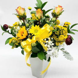 Yellow and white floral arrangement in a white vase with a yellow ribbon