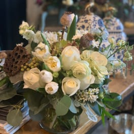 White floral arrangement in a glass vase with seed pods and greenery