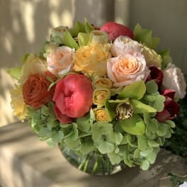 Mixed bouquet of peach, pink, and yellow flowers in a glass vase