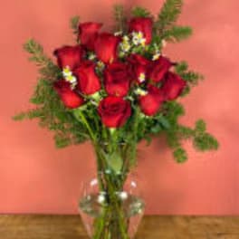 Red roses arranged in a clear glass vase with greenery