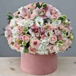 Round arrangement of soft pink and white flowers in a pink hat box container