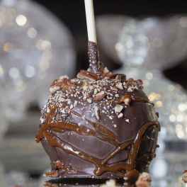 Chocolate dipped caramel apple on a stick, topped with chopped nuts and caramel drizzle