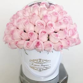 Round box of pale pink roses tightly arranged in a white hatbox with gold script label