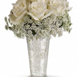 White roses arranged in a clear glass vase with delicate white filler flowers