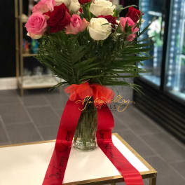 Bouquet of red, pink, and white roses in a glass vase with a red ribbon