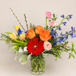 Mixed bouquet in a clear glass vase with orange, red, pink, yellow, and blue flowers