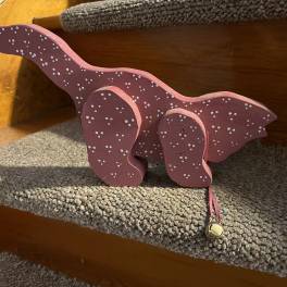 Pink wooden dinosaur decoration with white dots and a small bell