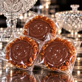 Three chocolate-covered treats wrapped in clear plastic on a reflective surface