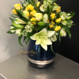 Yellow roses and white lilies arranged in a blue vase