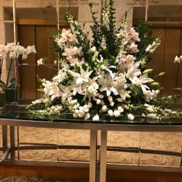 Large white floral arrangement with lilies and orchids on a table