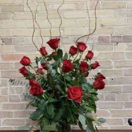 Tall bouquet of red roses in a glass vase with curly branches