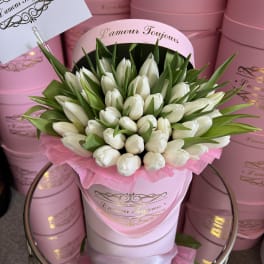 White tulips arranged in a pink hat box with green leaves