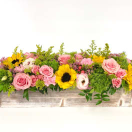 Low centerpiece of pink roses, yellow sunflowers, and green accents in a rustic whitewashed wooden box