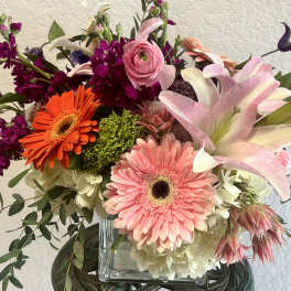 Mixed bouquet with pink lilies, gerbera daisies, and purple blooms in a glass vase