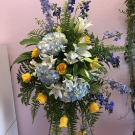 Standing floral spray with blue hydrangeas, white lilies, and yellow roses