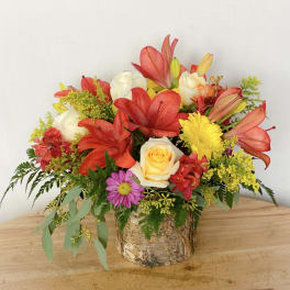 Colorful flower arrangement in a birch bark container with red lilies and roses