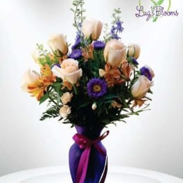 Bouquet of pale roses and purple flowers in a purple vase with ribbon