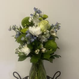 Bouquet of white, green, and blue flowers in a clear glass vase