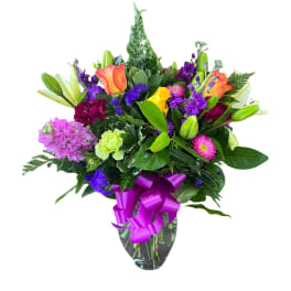 Mixed bouquet of colorful flowers in a glass vase with a purple ribbon