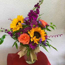 Bouquet of sunflowers, purple blooms, and orange roses in a glass vase