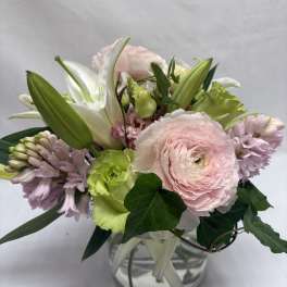 Pastel bouquet of pink ranunculus, lilies, and hyacinths in a round glass vase